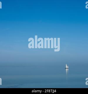 bateau à voile solitaire sur l'eau bleue d'un vaste lac vide sous le ciel bleu Banque D'Images