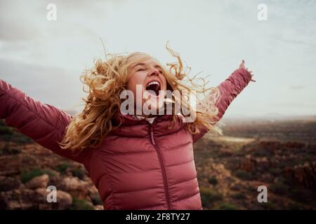 Gros plan d'une belle femme sur un sentier de montagne avec elle cheveux volants et mains étirées avec la bouche ouverte Banque D'Images