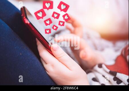 Concept des enfants et des réseaux sociaux. Petite fille tenant le téléphone avec amour comme coeur icônes de médias sociaux sur l'écran. Banque D'Images