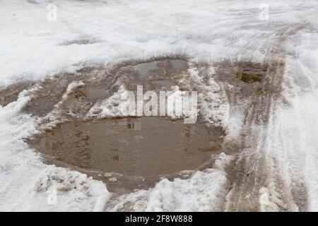 Chenilles pour roues et pneus de voiture sur une petite flaque de neige fondue. Concept de conditions météorologiques anormales. Il y a de l'espace de copie. Le nouvel an et les vacances de Noël sont terminé. Restes de neige de l'année dernière. Banque D'Images