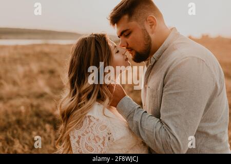 le mari embrasse sa femme en tenant sa main sur sa joue. Une famille heureuse se reposant dans la nature embrasse les baisers en été au coucher du soleil. Future mère prégnane caucasien Banque D'Images