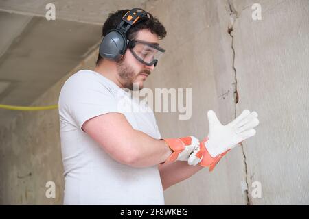 Builder enfilant des gants de protection, portant des lunettes de sécurité et des protections auditives. Sécurité au travail. Banque D'Images