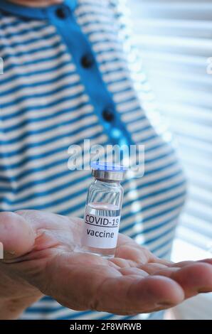 Vieille femme dans un t-shirt bleu tenant un flacon de vaccin flacon en verre pour la vaccination contre la pandémie du coronavirus COVID-19 SRAS-COV-2 dans ses mains. Banque D'Images