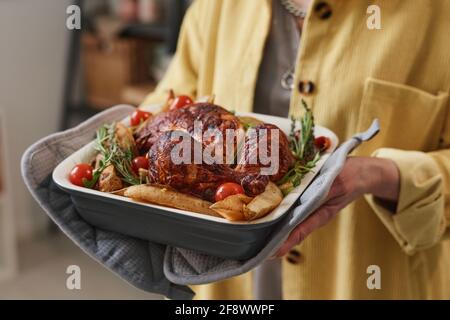 Gros plan d'une femme âgée tenant un plat avec du poulet rôti et légumes Banque D'Images