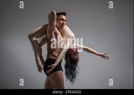 Posture du cirque intense. Un jeune homme tient une femme flexible. Deux acrobates ou danseurs de ballet se posant sur un fond blanc. Une paire de gymnastes exécutent l'art. Banque D'Images