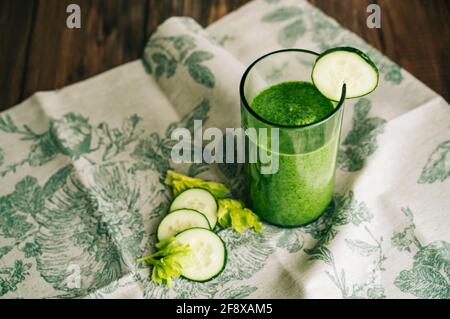 Vue aérienne d'un smoothie vert au céleri et au concombre en verre cristal sur un tissu gris de feuilles vertes sur une table en bois sombre Banque D'Images