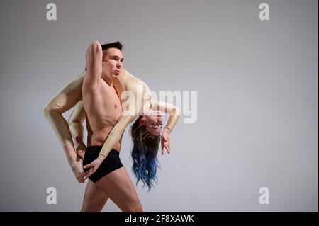 Posture du cirque intense. Un jeune homme tient une femme flexible. Deux acrobates ou danseurs de ballet se posant sur un fond blanc. Une paire de gymnastes exécutent l'art. Banque D'Images