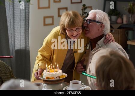 Heureux couple senior qui s'embrasse à la table tout en célébrant leur anniversaire avec gâteau à la maison Banque D'Images