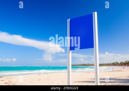 Un panneau d'affichage blanc bleu se dresse sur une plage tropicale vide par temps ensoleillé. Modèle de maquette de photo d'arrière-plan utile pour tout placement de texte et de panneaux dans cop Banque D'Images