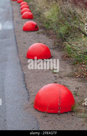 Des bollards en béton rouge anti-stationnement en forme d'hémisphère se tiennent dans une rangée le long un bord de route Banque D'Images