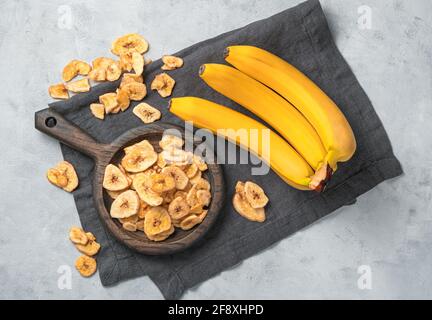 Fruit, dessert naturel : chips de banane. Morceaux de banane séchée et fruits frais sur fond gris. Vue de dessus. Banque D'Images