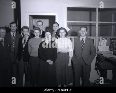 Dans les années 1950, historique, à l'intérieur d'un bureau d'entreprise, un groupe de fonctionnaires d'administration hommes et femmes se réunissent pour une photo, Angleterre, Royaume-Uni. À cette époque, le lieu de travail au bureau était formel et les employés devaient s'habiller d'une certaine manière. Pour les hommes comme pour les femmes, un costume en laine sur mesure élégant présentait une image professionnelle et aurait été le vêtement approprié dans un environnement de bureau d'entreprise à la fois. Comme on peut le voir, même le jeune lad, le bureau junior, porte une veste et une cravate. Banque D'Images