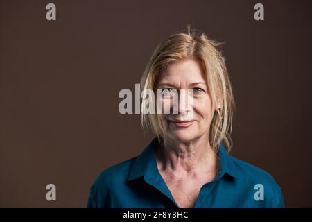 Gros plan d'une femme âgée aux cheveux blonds et en chemisier regarder la caméra isolée sur fond noir Banque D'Images