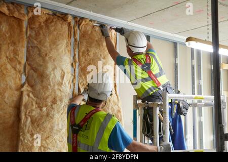 les ouvriers de la construction sur le chantier ajustent l'isolation au mur de clous Banque D'Images