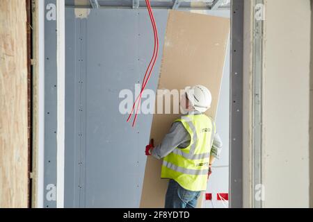 Le travailleur de la construction sur le chantier porte une feuille de plâtre Banque D'Images