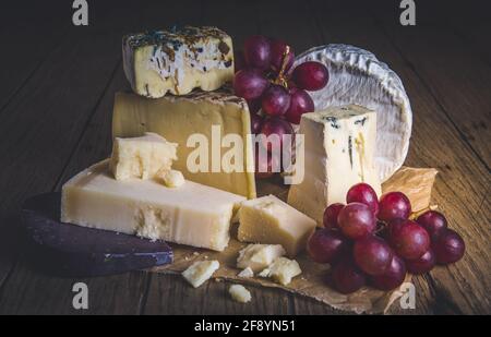 Variété de fromages exclusifs, décorés de raisins rouges, sur une table rustique en bois Banque D'Images
