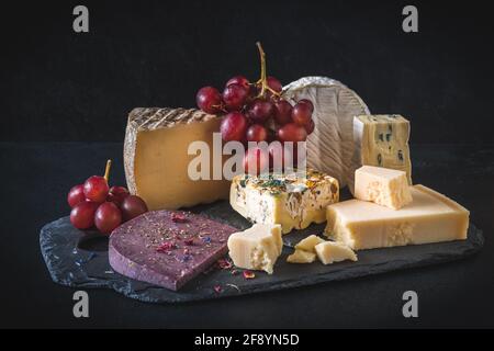 Variété de fromages exclusifs et colorés, décorés de raisins rouges, sur fond noir Banque D'Images