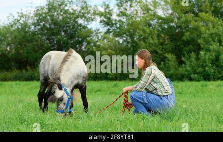 Jeune caucasienne et son poney affamé sur le terrain, vue latérale. Banque D'Images