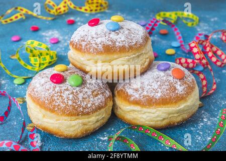 Krapfen, Berliner ou beignets avec des banderoles, des confettis et des grains de chocolat sur fond bleu. Image de carnaval ou d'anniversaire colorée. Banque D'Images