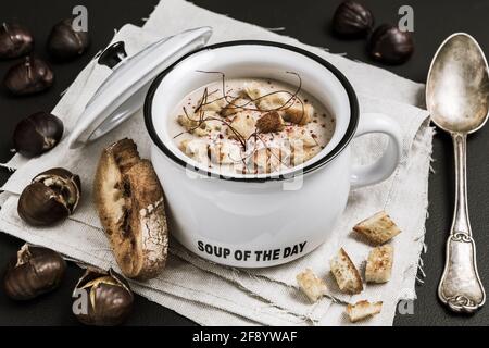 Soupe de châtaignes au parmesan, flocons de piment et fils dans un bol noir sur fond marron foncé, vertical avec espace de copie Banque D'Images