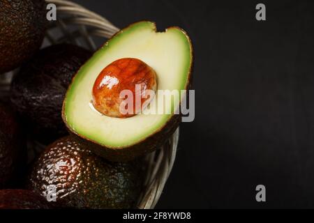 Avocats mûrs dans un panier sur une table noire, avec un fruit coupé et une pierre. Espace libre, vue de dessus Banque D'Images