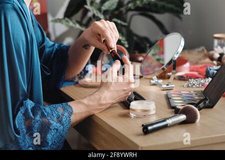 Gros plan d'un homme assis à la table et à l'aide d'un rouge à lèvres dans le maquillage pendant la préparation pour la performance Banque D'Images
