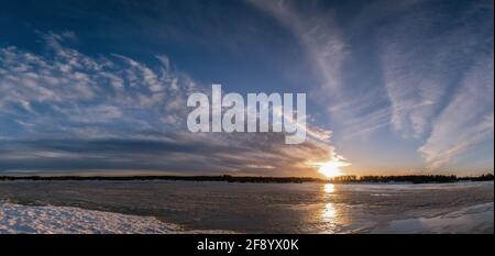 Panorama panoramique du coucher du soleil de printemps sur un lac glacial en fusion. Magnifique soleil rouge jaune orange, bleu foncé et nuages blancs sur ciel bleu. Northern Scand Banque D'Images