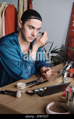 Jeune homme transgenre appliquant le maquillage à la table qu'il applique mascara sur les yeux Banque D'Images