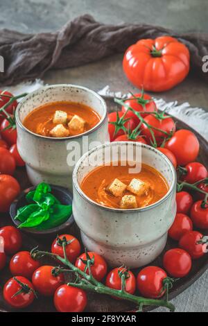 Deux tasses remplies de soupe de tomates maison sur une assiette en bois avec une variété de tomates mûres, verticales Banque D'Images