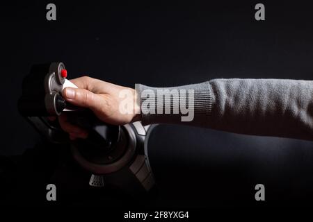 Main masculine jouant au jeu de tir d'avion avec joystick sur fond noir. Banque D'Images