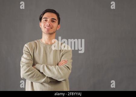 Jeune homme souriant avec bras pliés sur fond gris Banque D'Images