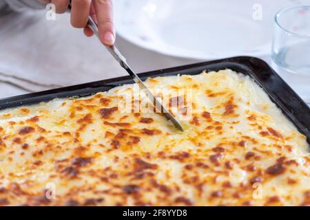 couteau à couper des cannelloni au gratin avec sauce béchamel sur un plateau Banque D'Images