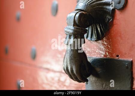 Ancien knocker en métal en forme de main sur une porte en bois cloutée peint en rouge Banque D'Images