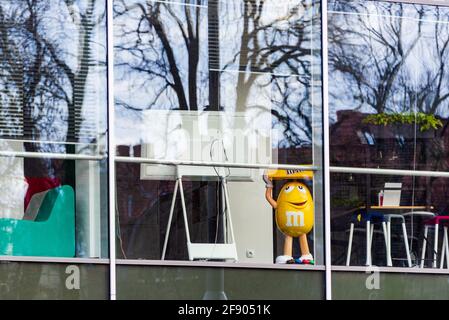 La grande figure jaune de M M dans un immeuble de bureaux vide pendant la pandémie du virus corona. Il s'agit d'une mascotte de caractère de la marque de chocolat m&m's pro Banque D'Images