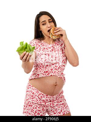 Femme enceinte qui choisit entre une laitue et un hamburger, isolée sur fond blanc