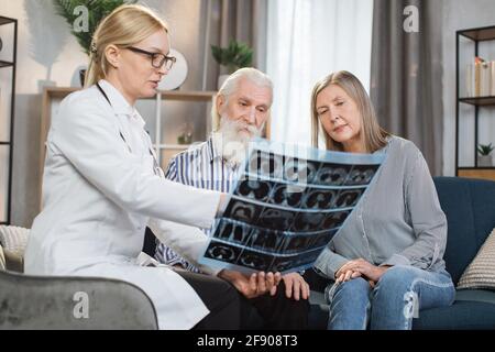 Portrait d'un couple senior satisfait et positif, regardant la radiographie et écoutant un médecin professionnel et confiant, en leur rendant visite à la maison et en parlant de l'état des poumons Banque D'Images