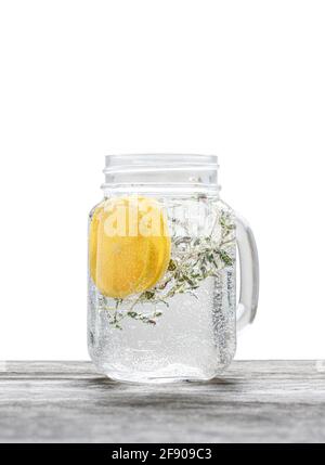 Eau pétillante avec tranches de citron et feuilles de thym en verre pot isolé sur blanc Banque D'Images