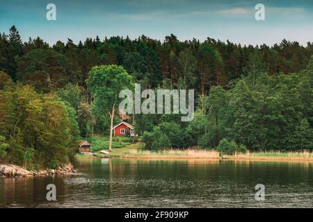 Suède. Magnifique cabane en bois rouge suédois sur la côte des Rocheuses en été. Paysage de lac ou de rivière et de forêt Banque D'Images