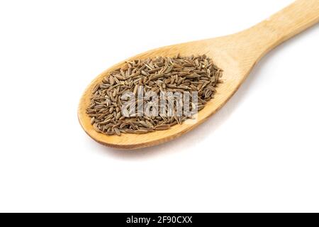 Gros plan des graines de cumin sur une cuillère en bois isolée sur fond blanc. Banque D'Images