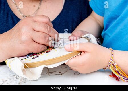 Gros plan des mains d'une fille et de sa grand-mère faire un embroide Banque D'Images