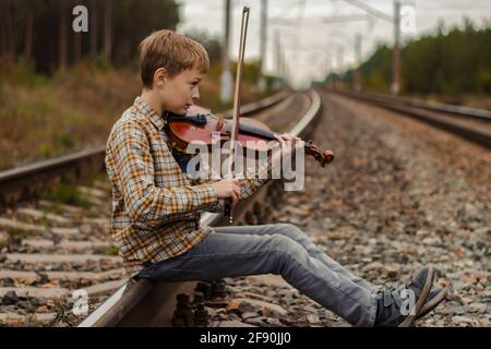 Un beau garçon blond est assis sur les rails du chemin de fer et joue le v Banque D'Images