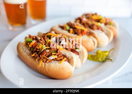 Gros plan sur une assiette de chiens Chili avec des verres de bière en arrière-plan. Banque D'Images