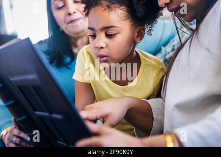 Jolie fille regardant un album photo tout en étant assise avec la famille à la maison Banque D'Images