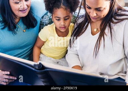 Famille de plusieurs générations regardant un album photo tout en étant assis accueil Banque D'Images
