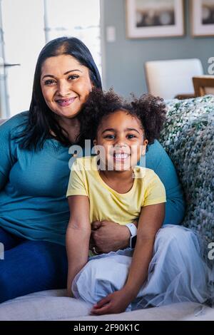 Portrait d'une petite fille souriante assise avec grand-mère sur un canapé à la maison Banque D'Images