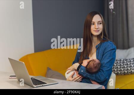 Belle jeune mère travaillant avec un ordinateur portable et allaitant, tenant et allaitant son nouveau-né à la maison. Maman - femme d'affaires nourrissant newb Banque D'Images