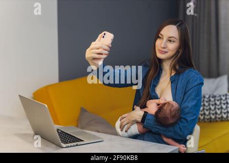 Belle jeune mère travaillant avec un ordinateur portable et allaitant, tenant et allaitant son nouveau-né à la maison. Maman - femme d'affaires nourrissant newb Banque D'Images