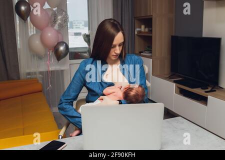 Belle jeune mère travaillant avec un ordinateur portable et allaitant, tenant et allaitant son nouveau-né à la maison. Maman - femme d'affaires nourrissant newb Banque D'Images