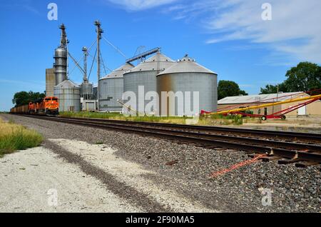 Altona, Illinois, États-Unis. Un train de marchandises de Burlington Northern Santa Fe passe devant des réservoirs de stockage d'une coopérative agricole. Banque D'Images