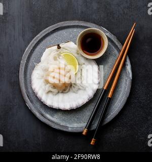 Sashimi de pétoncles vivants en carapace avec du daïkon, de la lime et de la sauce soja sur fond sombre Banque D'Images